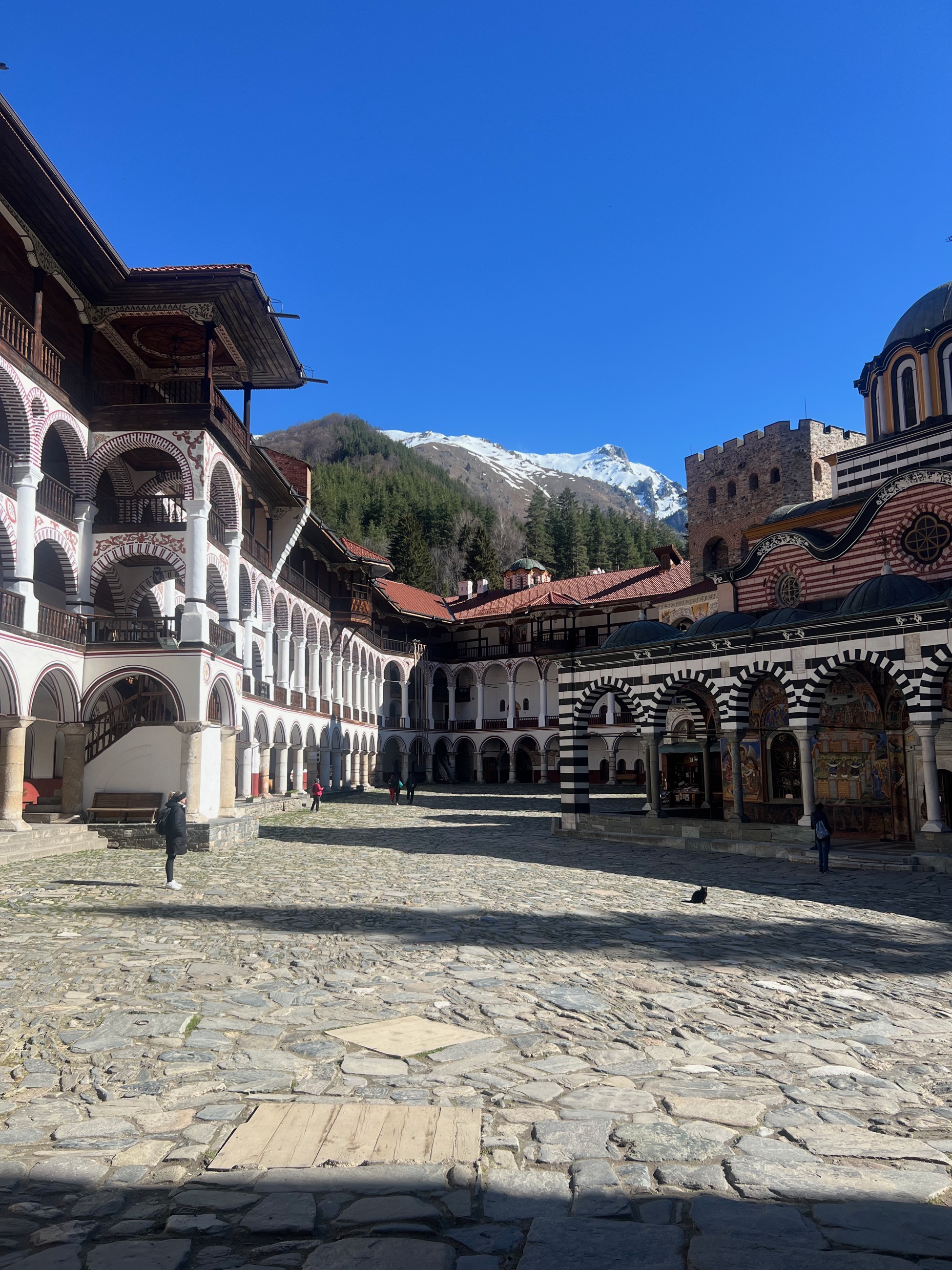 The striped arcades of Rila Monastery under a snowy peak